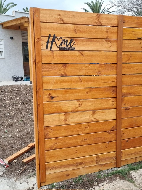 שלט Home עם שם משפחה על גדר עץ