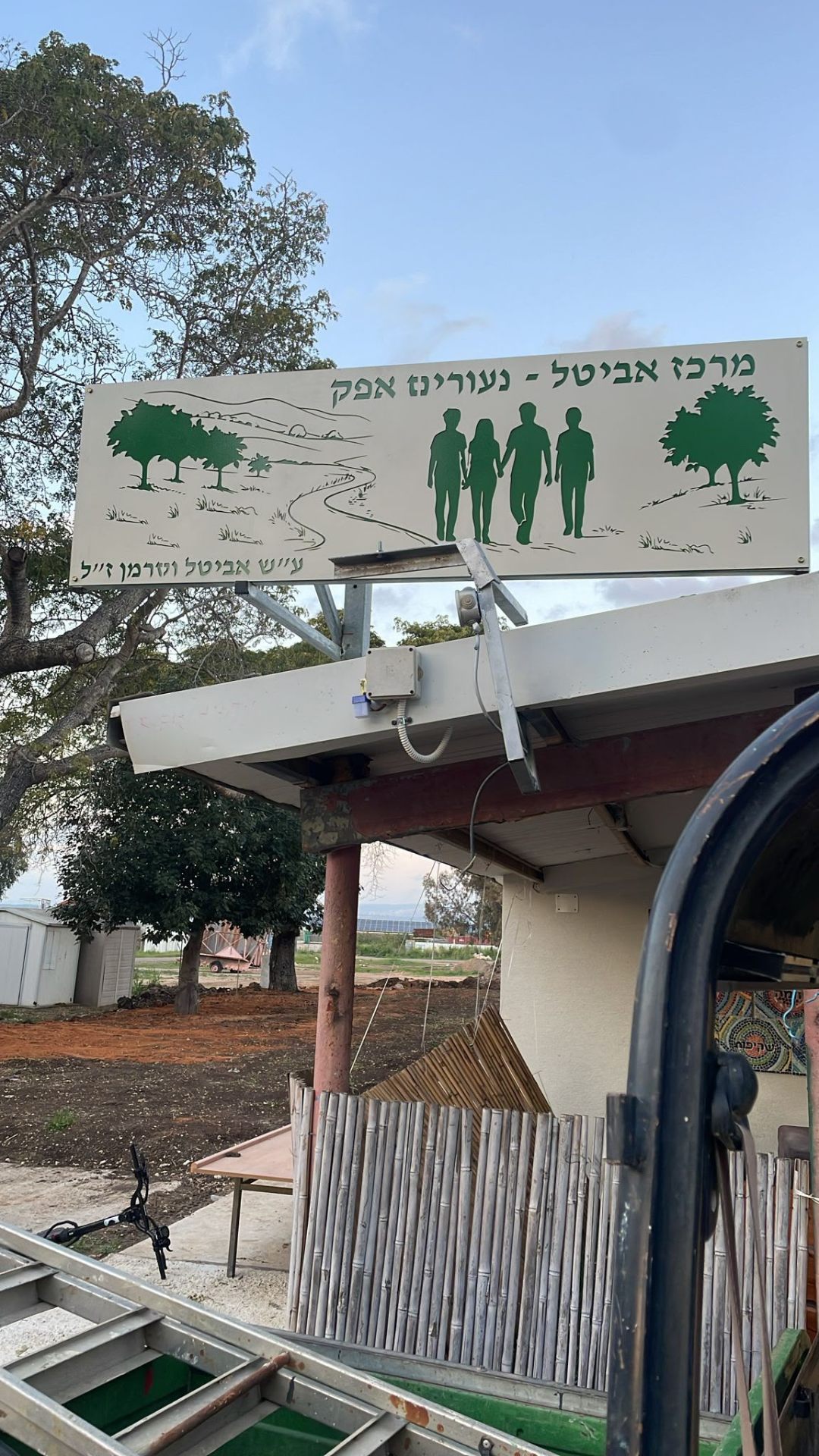 שלט מתכת גדול בהדפסה ירוקה עם עצים ודמויות מעל מבנה