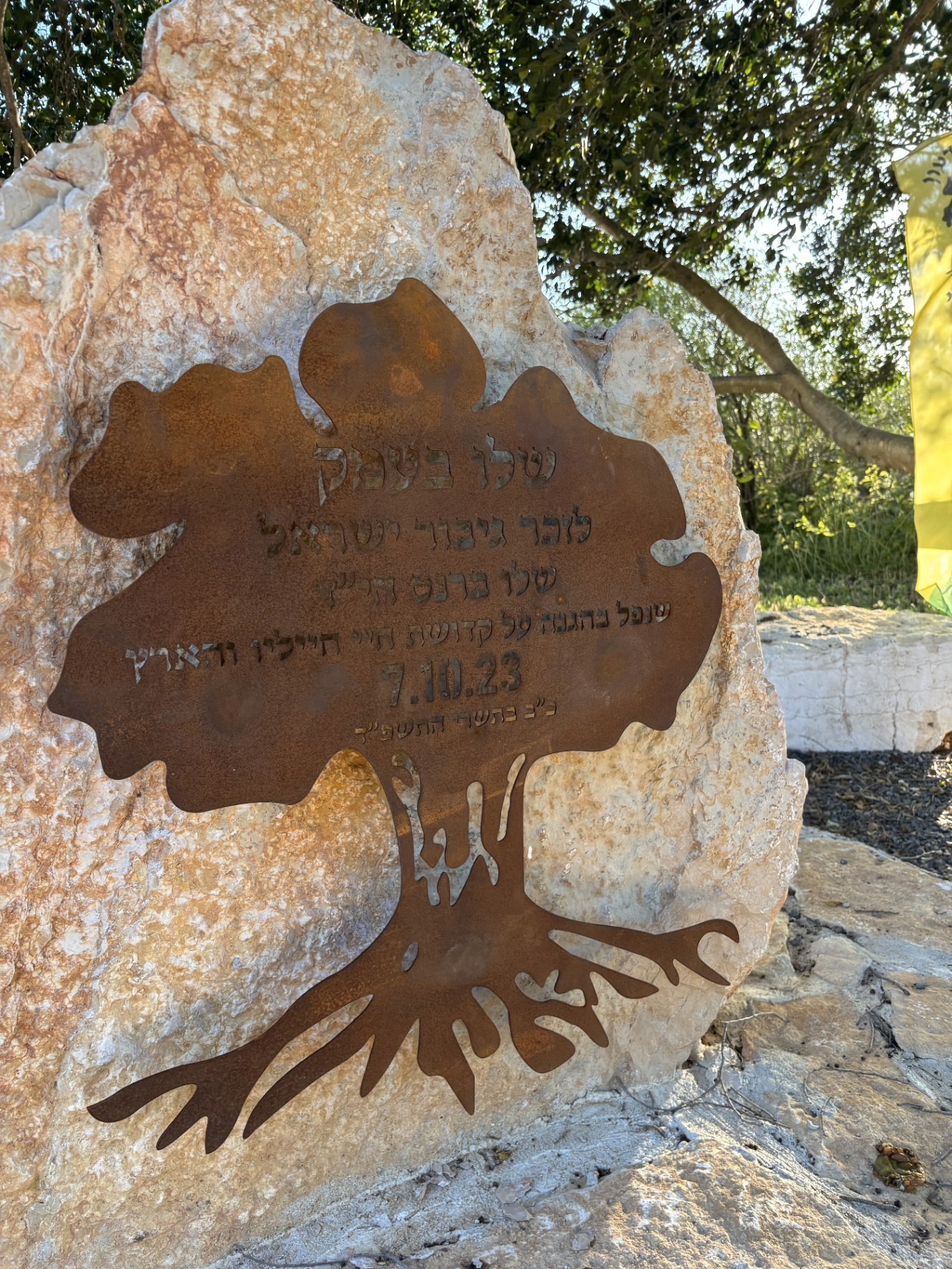 שלט הנצחה בצורת עץ מקורטן על סלע אבן
