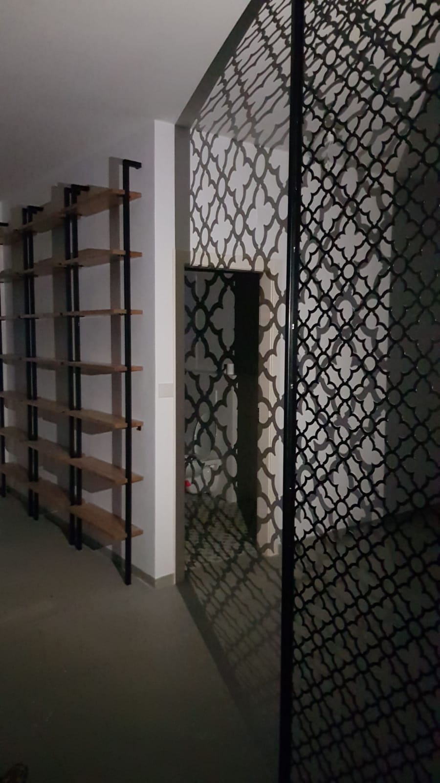 מבט צד על משרבייה שחורה בדוגמה מרוקאית ליד מדפי עץ, עם צללי הדוגמה