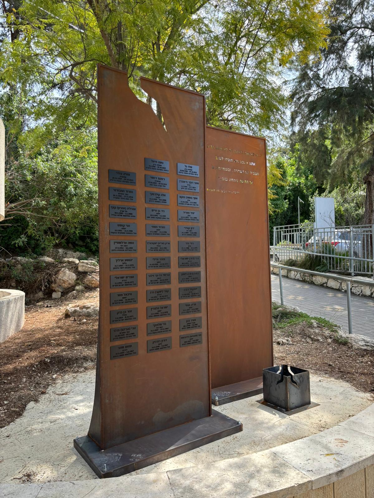 אנדרטת קורטן עם לוחיות שמות הנופלים וכיתוב שיר, בגן הנצחה מוצל
